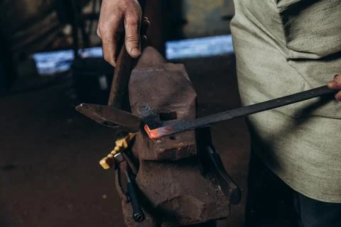 The blacksmith manually forging the red-hot metal on the anvil in smithy. Stock Photos