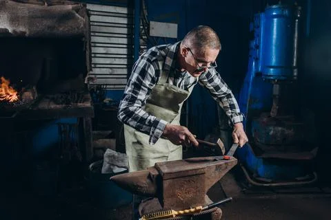 The blacksmith manually forging the red-hot metal on the anvil in smithy. Foto stock