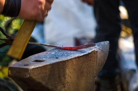 Blacksmith performs the forging of hot glowing metal on the anvil Stock Photos
