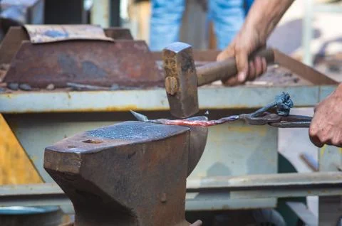 Blacksmith performs the forging of hot glowing metal on the anvil Stock Photos