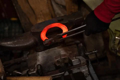 Blacksmith performs the forging of hot glowing horseshoe on the anvil Stock Photos