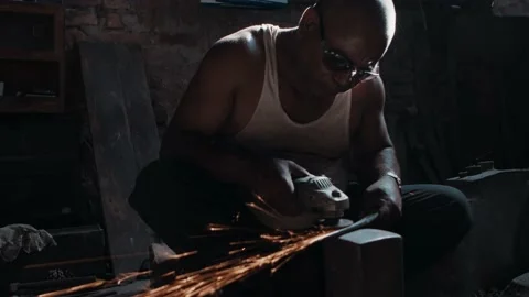 Blacksmith polishing knife blade using grinder, sparks flying Stock Footage 166846115