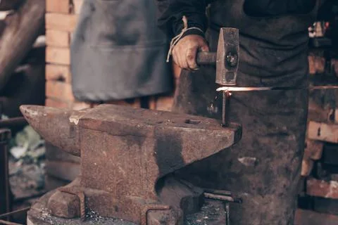 Blacksmith process glowing metal with hammer on anvil in forge. Dirty hands of Stock Photos