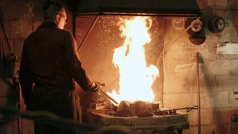 Blacksmith pulls a glowing knife blade out of the burning furnace. Metalworking Stock Footage 143382865