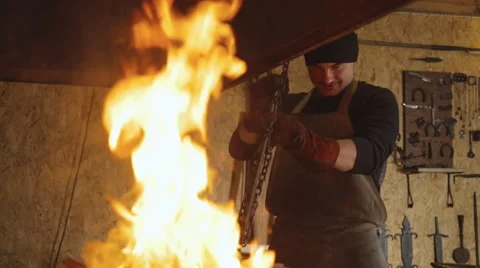 Blacksmith puts metal billet on chain in furnace to heat it Stock Footage 64334846