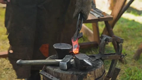 A blacksmith shapes a piece of red-hot metal using tongs and a hammer. The Vidéo 345036926