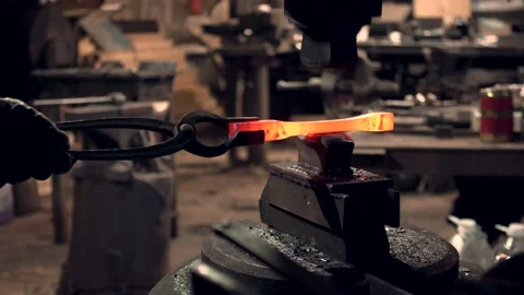 Blacksmith shaping hot iron bar working with a large industrial hammer Stock Footage 132653080