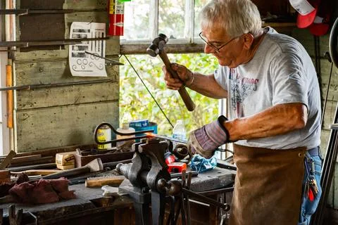 Blacksmith is using hammer to forge metal in a workshop in Maine Stock Photos