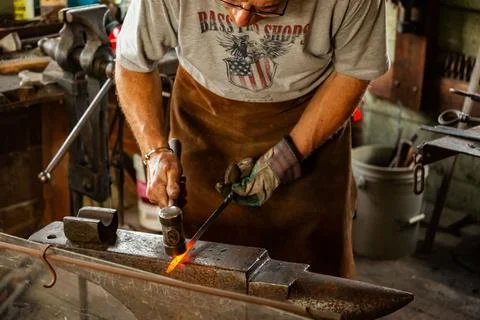 Blacksmith is using hammer to forge metal in a workshop in Maine Stock Photos