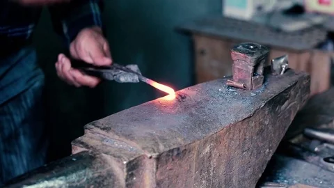 Blacksmith work. Blacksmith beats a piece of white hot metal with a hammer on an Stock Footage 76373536