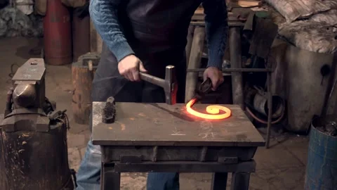 Blacksmith working with a hammer shaping a hot red iron twirl Stock Footage 132653166