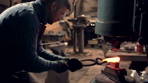 Blacksmith working hot iron bar with a large industrial hammer Stock Footage 132653009