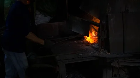 Blacksmith working in a smithery putting charcoal in a furnace oven Stock Footage 71391743