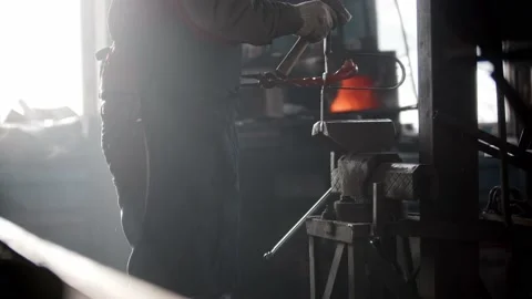 Blacksmith workshop - a man puts heated metal detail in the pressing retainer Stock Footage 180498519