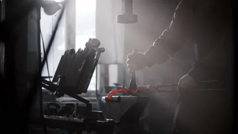 Blacksmith workshop - a man shaping heated metal on an anvil using a form and Stock Footage 180505098