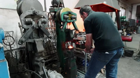 A blacksmith in a workshop works with metal and an automatic hammer. Stock Footage 231700429