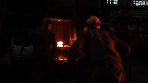 Blacksmiths in a helmet put a piece of hot metal under a mechanical hammer on an Stock Footage 143320528