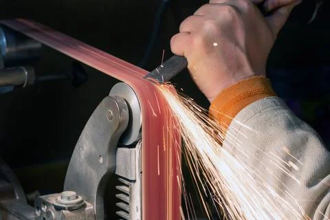 Blade sharpening creating on a belt grinder process. Knife making master hand Foto stock