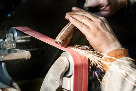 Blade sharpening creating on a belt grinder process. Knife making master hand Foto stock