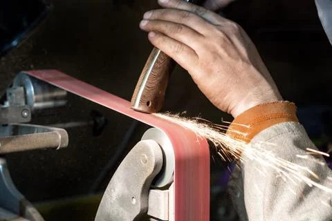 Blade sharpening creating on a belt grinder process. Knife making master hand Stock Photos