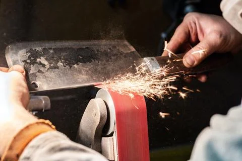 Blade sharpening creating on a belt grinder process. Knife making master hand Stock Photos