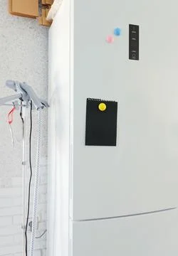 Blank black note board with magnets on refrigerator in kitchen. Mockup for Stock Photos