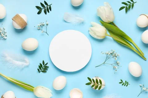 Blank card with Easter eggs, flowers, leaves and feathers on blue background Stock Photos