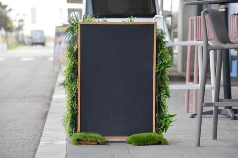 Blank chalkboard menu outside cafe framed by green plants - eco, Earth Day an Stock Photos