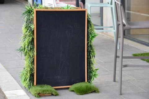 Blank chalkboard menu outside cafe framed by green plants - eco, Earth Day an Stock Photos