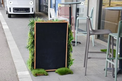 Blank chalkboard menu outside cafe framed by green plants - eco, Earth Day an Stock Photos