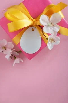 Blank egg-shaped gift label on pink gift box with apple branch and yellow r.. Stock Photos