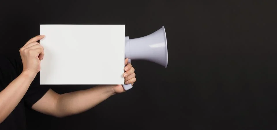 Blank empty paper in man's hand with megaphone on black background. Stock Photos