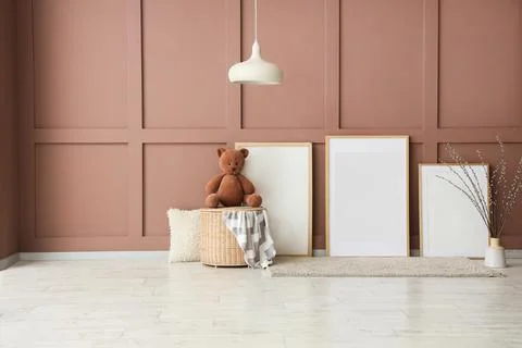 Blank frames with basket, toy bear and willow branches near brown wall in chi Фото