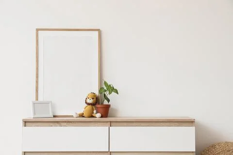 Blank frames with toy lion and plant on chest of drawers near light wall Фото