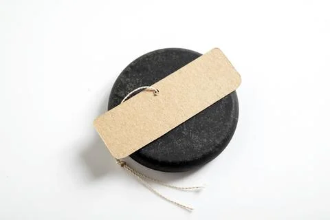 Blank kraft paper tag with string resting on a round black stone, isolated .. Stock Photos