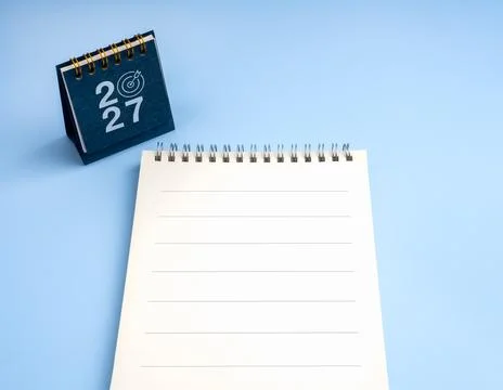 Blank lined notebook beside 2027 desk calendar with target symbol on blue b.. Stock Photos