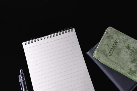 Blank lined spiral notepad pen and stacked closed notebooks on black backgrou Stock Photos