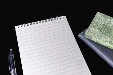 Blank lined spiral notepad pen and stacked closed notebooks on black backgrou Stock Photos