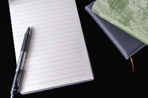 Blank lined spiral notepad pen and stacked closed notebooks on black backgrou Stock Photos