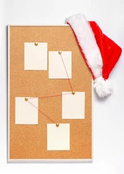 Blank note sheets are pinned to the board. Santa's hat on a cork board. Stock Photos