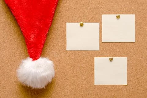 Blank note sheets are pinned to the board. Santas hat on a cork board. Stock Photos