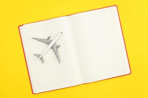 Blank notebook and airplane model on yellow background, flat lay. Stock Photos