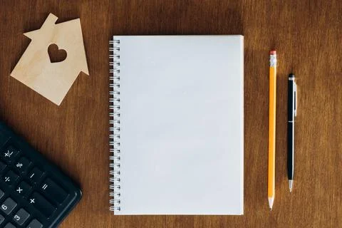 Blank notebook, calculator and model of a house on a wooden table, flat lay. Stock Photos