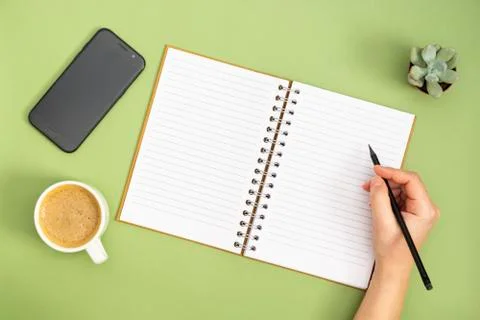 Blank notebook with empty page, coffee cup and hand holding a pencil. Table t Stock Photos