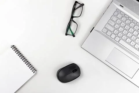 A blank notebook with glasses a computer mouse and a laptop are on a white ta Stock Photos