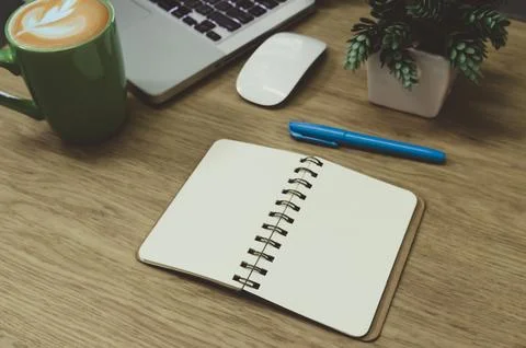 Blank notebook lying on a wooden table and a green coffee mug on the computer Photos