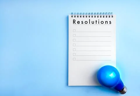 Blank notebook with Resolutions title, checklist and blue light bulb on pas.. Stock Photos