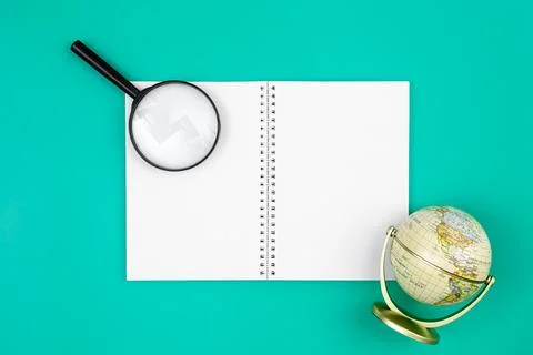 Blank notepad, globe and magnifier on a blue background, copy space. Stock Photos
