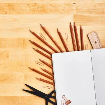 Blank notepad over school and office supplies on yellow wooden table. Stock Photos