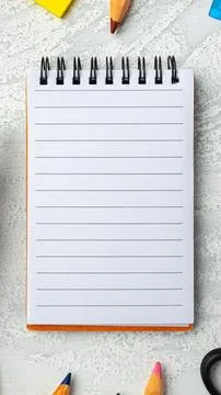 Blank notepad on a table with colored pencils and sticky notes nearby Stock Photos